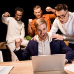 Essential LMS Features to Improve Online Learning Outcomes happy multicultural businesspeople showing winner gesture while working at night in office