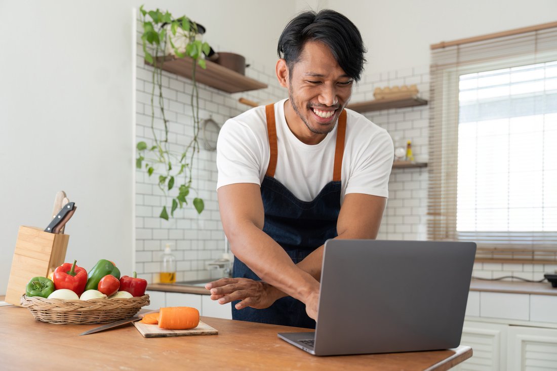 man in kitchen looking at recipes on laptop while pcv6sly.jpg